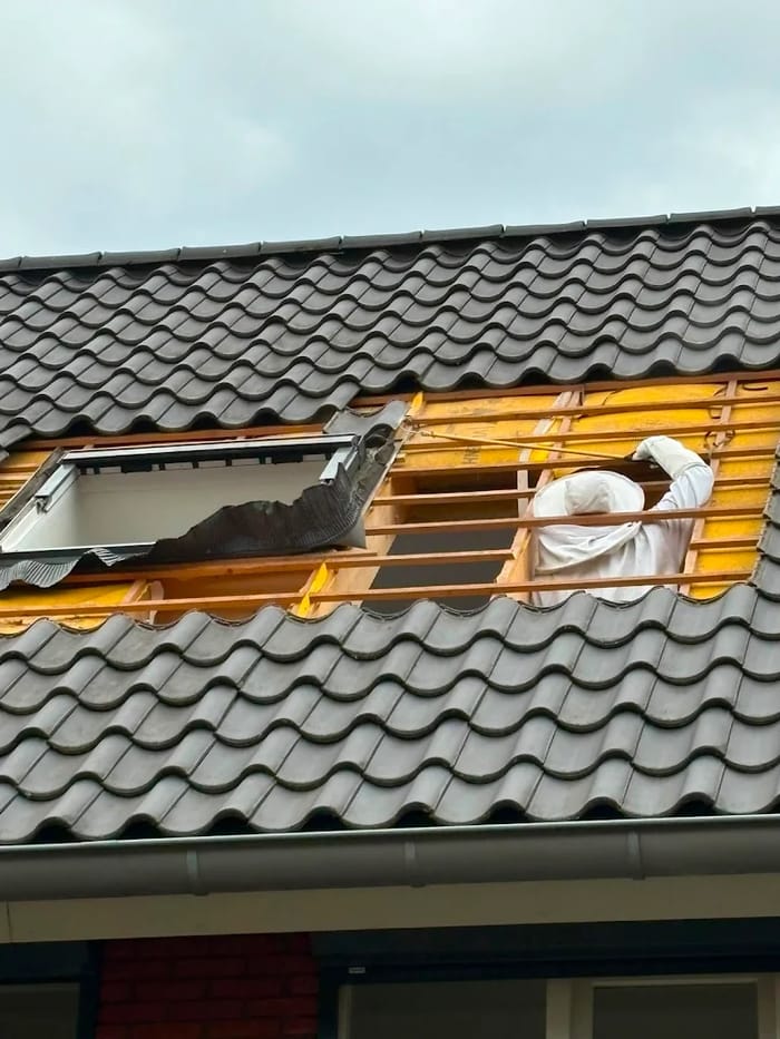 Specialist in beschermend pak verwijdert dakpannen voor een wespennest onder het dak